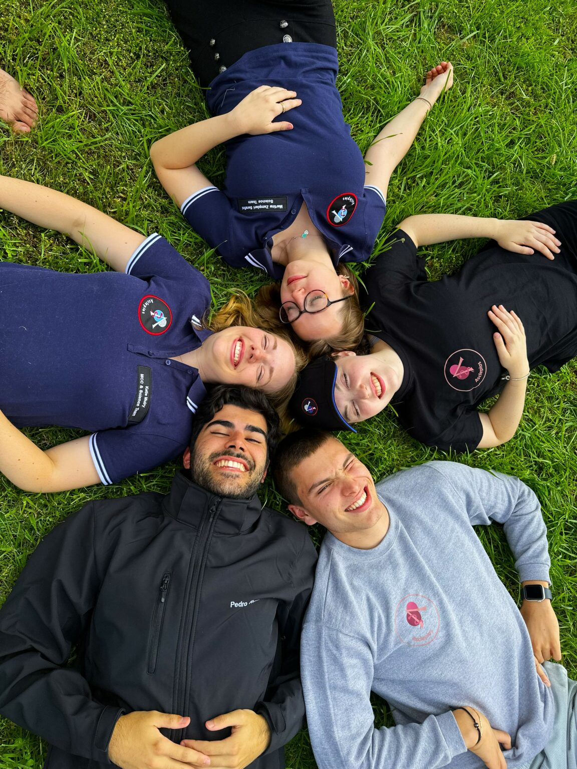 Five members of the crew lying in a circle on the grass in Asclepios polo shirts and sweatshirts